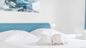 Una cama bien hecha con sábanas blancas y dos toallas dobladas en la cabecera.