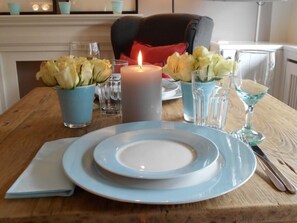 Une table à manger dressée avec des assiettes bleues, une bougie et deux vases ornés de fleurs.