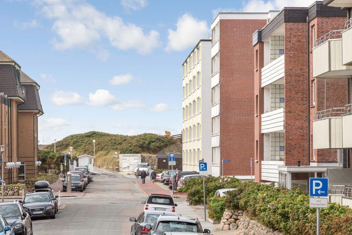 Eine Straße mit parkenden Autos, einem Parkschild und einem mehrstöckigen Gebäude mit Balkonen.