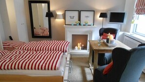 Hotellihuone, jossa on kaksi sänkyä, takka, kynttilöillä koristeltu pöytä, tuoli ja televisio.