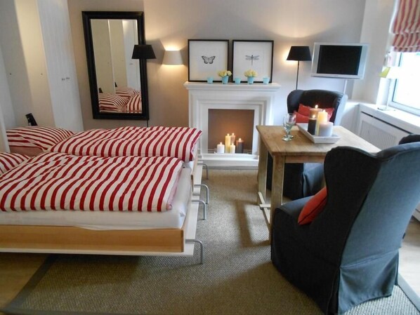 A hotel room with two beds, a fireplace, a table with candles, a chair, and a TV.