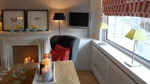 Tunnelmallinen olohuone, jossa on takka, televisio ja ikkuna, jossa on raidalliset verhot.