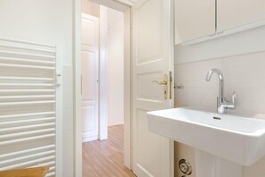 A bathroom with a white sink, a mirror, and a door leading to another room. - Ruhig. Edel. Garten. Haus Mühlenhof, Whg. 4 Objekt-id: Mht/04 (Westerland)