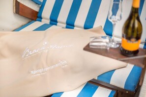 A beige bag with text on it, a bottle of wine, and a glass on a striped blue and white couch. - Ruhig. Edel. Garten. Haus Mühlenhof, Whg. 4 Objekt-id: Mht/04 (Westerland)