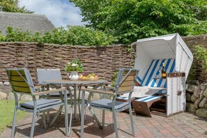 An outdoor seating area with a table, chairs, and a wicker basket containing fruits and a vase. - Ruhig. Edel. Garten. Haus Mühlenhof, Whg. 4 Objekt-id: Mht/04 (Westerland)