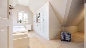Un dormitorio con cama, ventana, armarios blancos y un pequeño reposapiés.