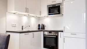 Cocina moderna con muebles blancos, horno empotrado, microondas y cafetera.