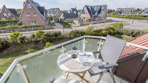 Un balcón con una mesa y sillas de vidrio, con vistas a una zona residencial con casas y una calle.
