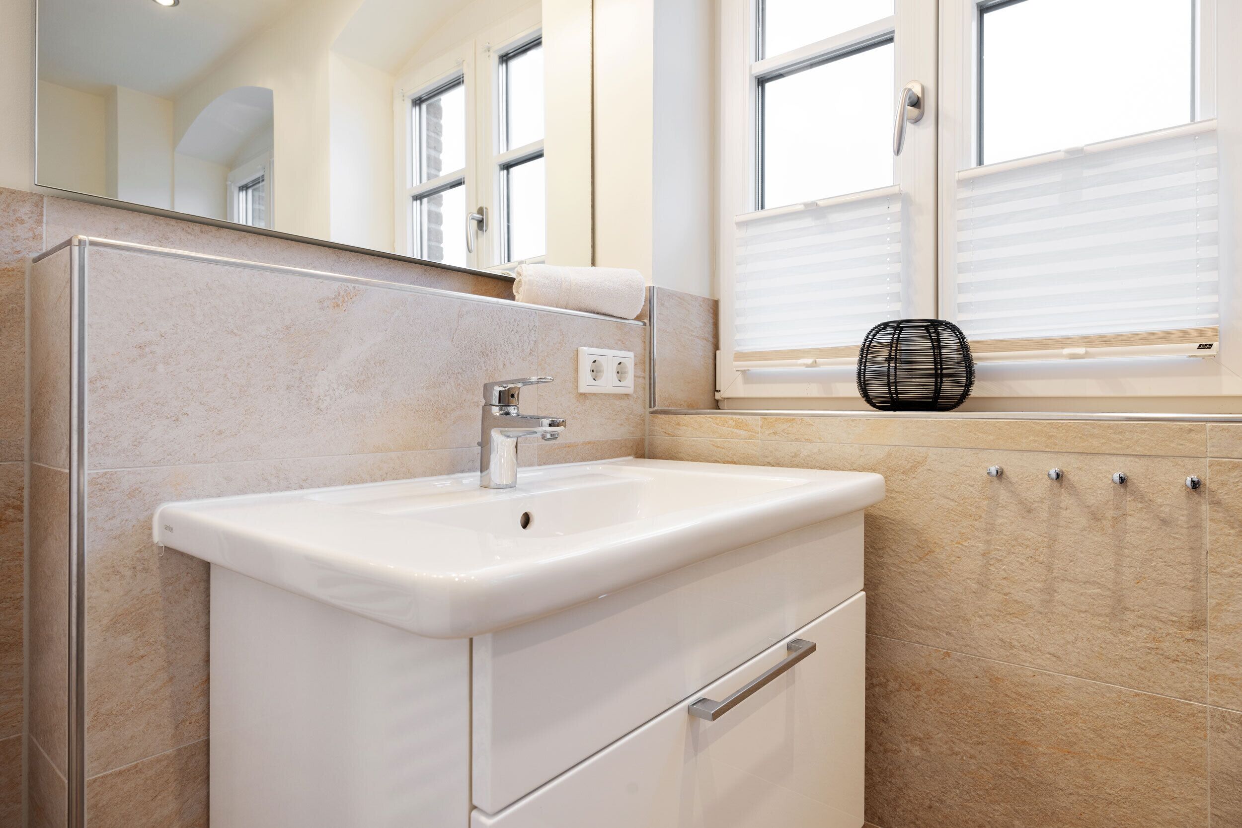 A bathroom with a white sink, a mirror, and a window with blinds.