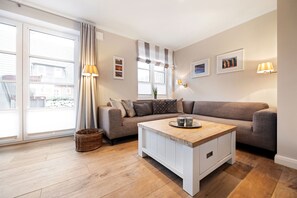 En moderne stue med sofa, sofabord og et stort vindue med gardiner.