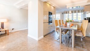 Una cocina moderna con electrodomésticos de acero inoxidable, una zona de comedor con mesa y sillas, y ventanas amplias que ofrecen luz natural.
