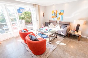 A living room with a glass-top coffee table, two red armchairs, a grey sofa, and a painting on the wall.