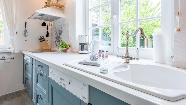 A modern kitchen with a large window, white cabinetry, and a built-in sink. - Behaglich. Britisch. Zuhause (Westerland)