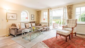 A living room with a sofa, armchair, coffee table, and a red patterned rug. - Behaglich. Britisch. Zuhause (Westerland)