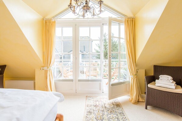 A bedroom with a large window, a chandelier, a wicker chair, and a bed.