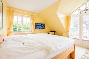 A bedroom with a large bed, a television on the wall, and a window with curtains.