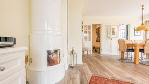 A modern kitchen with a central white stove, a dining area with a wooden table and chairs, and a hallway leading to other rooms. - Behaglich. Britisch. Zuhause (Westerland)