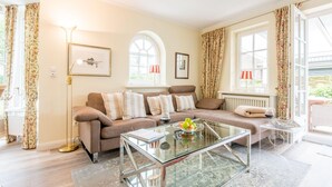 A cozy living room with a sofa, a glass coffee table, and a radiator. - Behaglich. Britisch. Zuhause (Westerland)