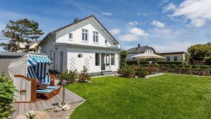 A white house with a large front porch, a covered outdoor seating area, and a well-maintained lawn. - Bäderstil. Strand. Sauna. Objekt-id: Ebw/48 (Westerland)