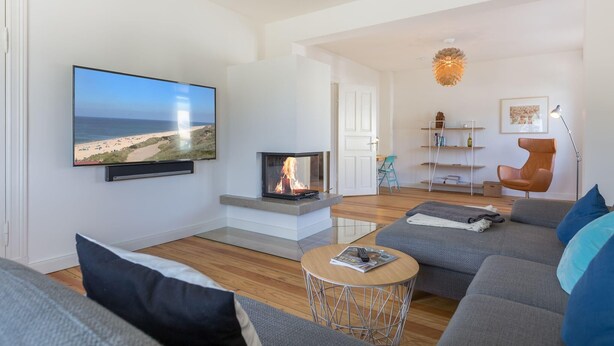 A modern living room with a fireplace, a large flat-screen TV, a sofa, and a coffee table. - Bäderstil. Strand. Sauna. Objekt-id: Ebw/48 (Westerland)