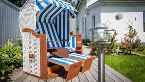 A wicker beach chair with a striped canopy, a wooden table, and a metal lamp post. - Bäderstil. Strand. Sauna. Objekt-id: Ebw/48 (Westerland)