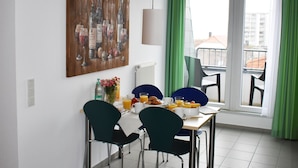 A dining area with a table, chairs, a painting, and a view of the outside. - Posthus Apartment 303 with balcony, close to the beach and central (Borkum)