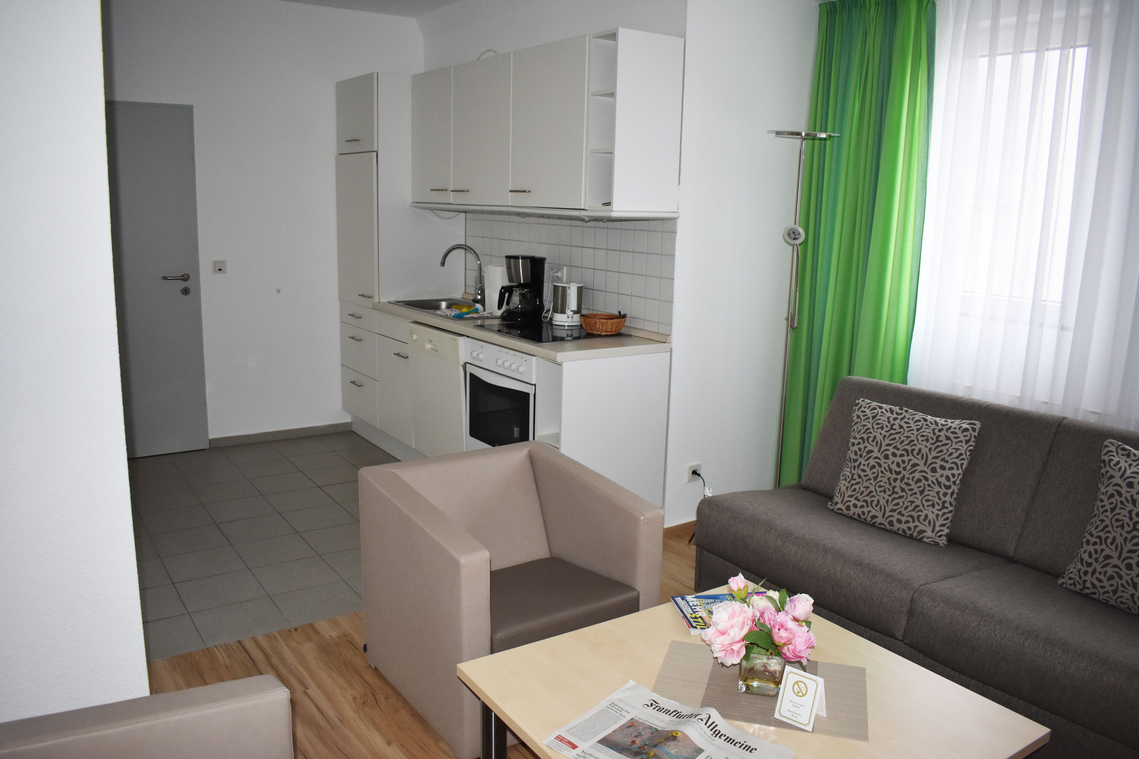 A compact living space with a kitchenette, a sofa, a small armchair, and a table with a vase of flowers. - Posthus Apartment 303 with balcony, close to the beach and central (Borkum)