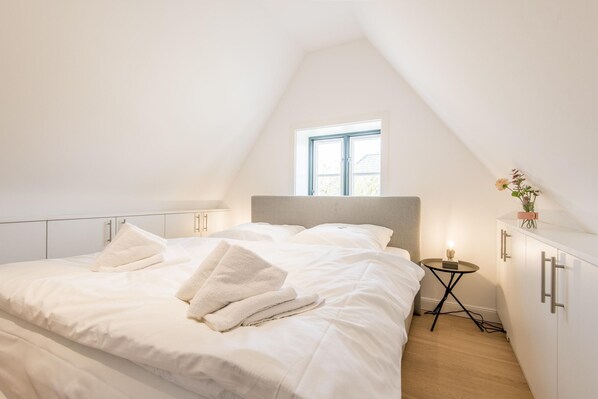A bedroom with a large bed, a small bedside table, and a window.