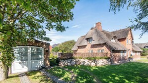 Ett traditionellt hus byggt av tegel med ett halmtak, en stenmur och en asfalterad uppfart.