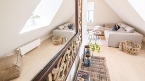 En rymlig loftlägenhet med högt i tak, ett stort fönster och en mysig sittgrupp med en soffa och fåtöljer.