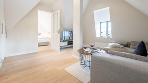 En modern lägenhet i loftstil med högt i tak, en matplats med ett glasbord, en soffa och en tv i bakgrunden.