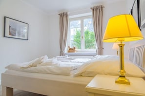 Un lit bien fait, avec du linge de lit blanc, une lampe de chevet et une fenêtre avec des rideaux.