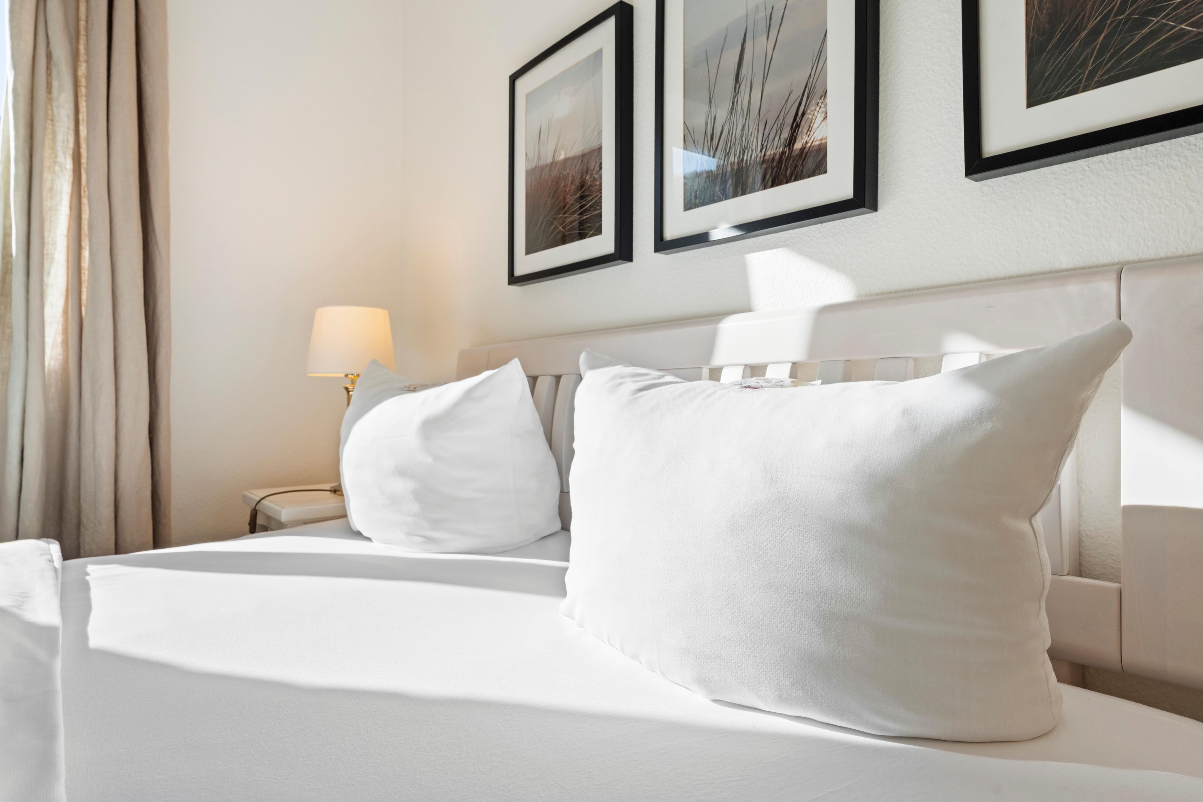 A hotel room with a neatly made bed, a bedside lamp, and framed pictures on the wall.