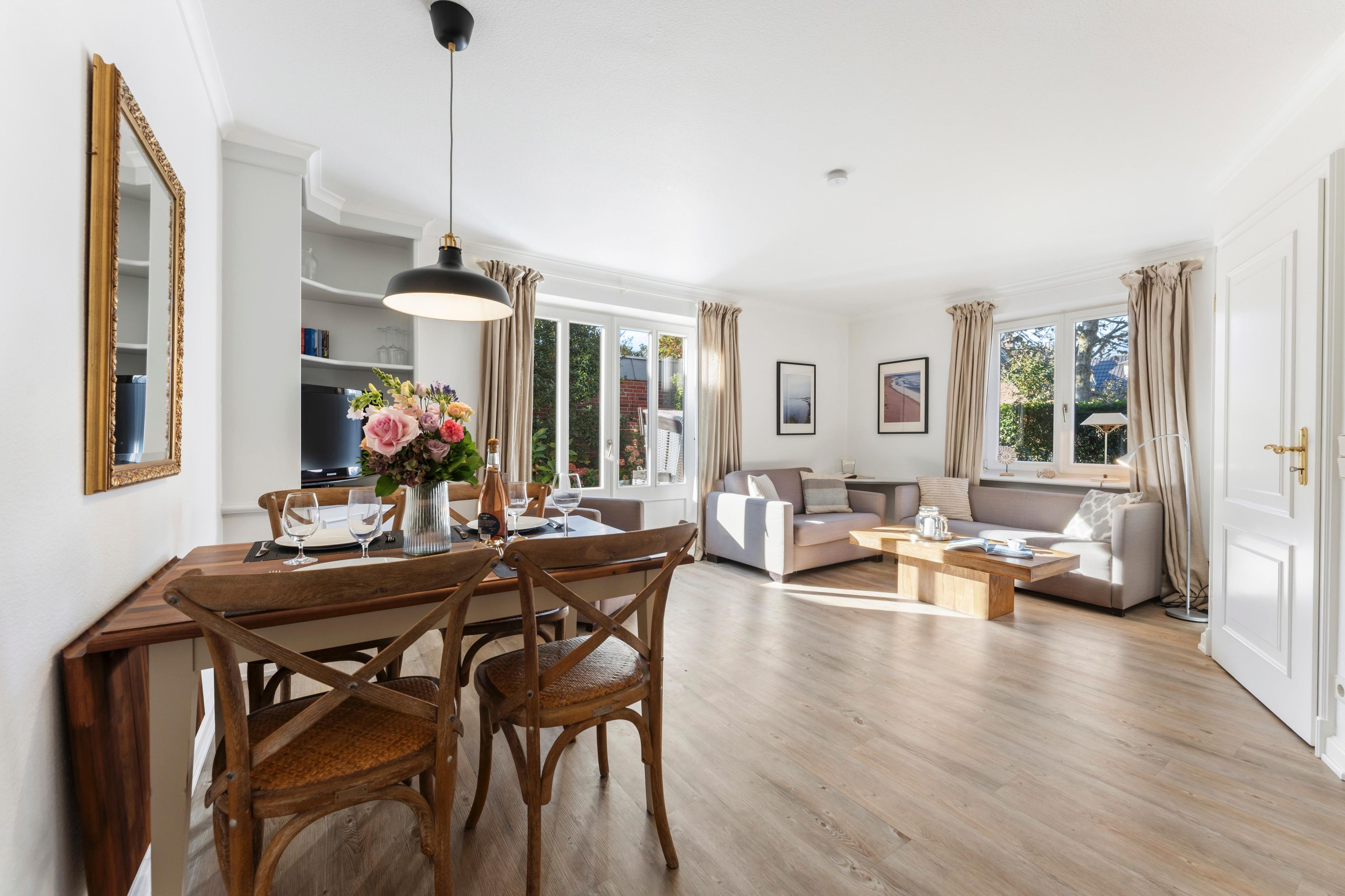 A spacious living room with a dining area, large windows, and a modern chandelier.