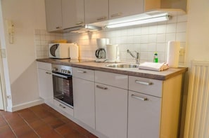 Une cuisine compacte avec des meubles blancs, un four encastré, un four à micro-ondes, une machine à café et un évier.