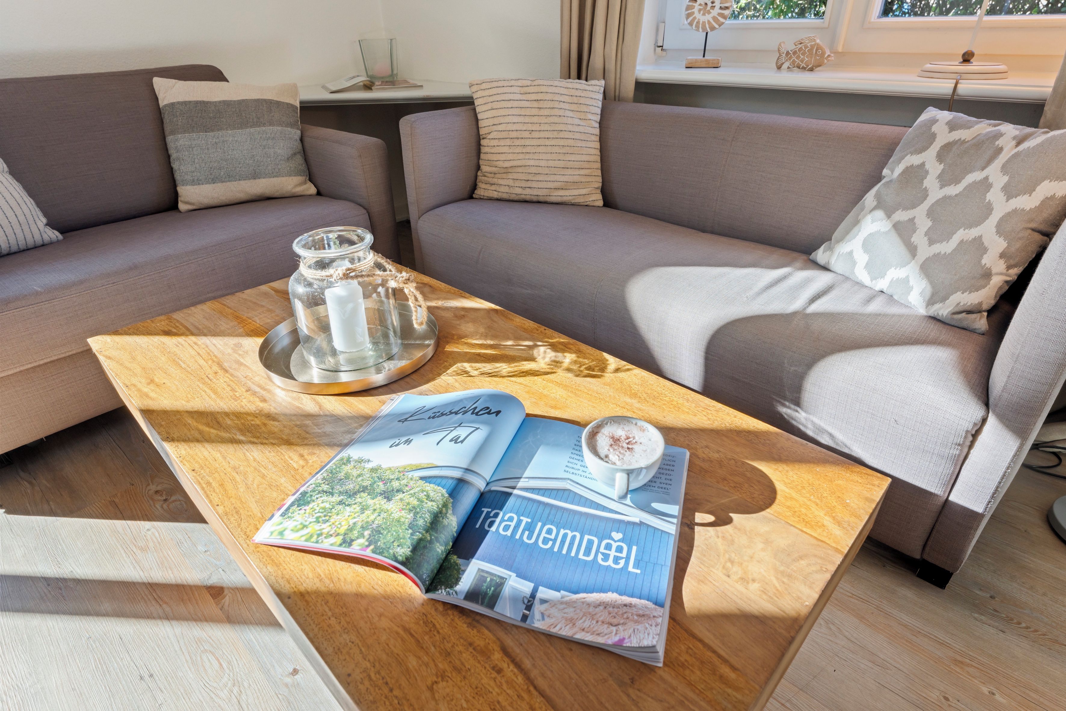 Uma sala de estar com sofá, mesa de centro, revista, pote de vidro e xícara de café.