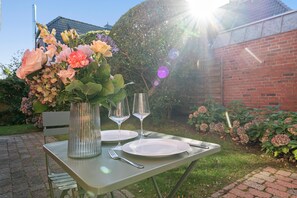 An outdoor dining table with a vase of flowers, two wine glasses, and cutlery. - Gemütlich. Strandkorb. Ruhig. Senwai-hüs, Whg. 2 "keitum" Objekt-id: Hsw/02 (Westerland)