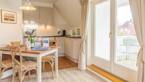 Een keuken met witte kasten, een eettafel met stoelen, een hanglamp en uitzicht door een schuifdeur naar buiten.