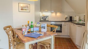 Een kleine keuken met een eettafel, stoelen en eenvoudige apparaten.