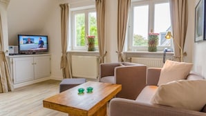 Een woonkamer met een televisie, een bank, een tafel en een raam met gordijnen.