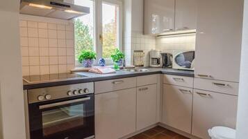 A modern kitchen with white cabinets, a built-in oven, a microwave, and a window with potted plants.