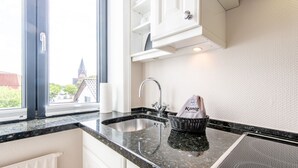 Cozinha com bancada de granito, pia de aço inoxidável, cesta com um saco e vista para edifícios.