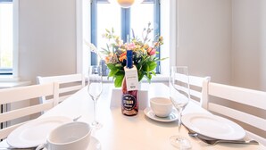 A dining table set with white plates, bowls, and cutlery, a bottle of wine, and a vase of flowers. - Stadthaus Boysenstraße, Whg. 7 Ruhig. Gemütlich. Strandnah. Objekt-id: Shb/07 (Westerland)