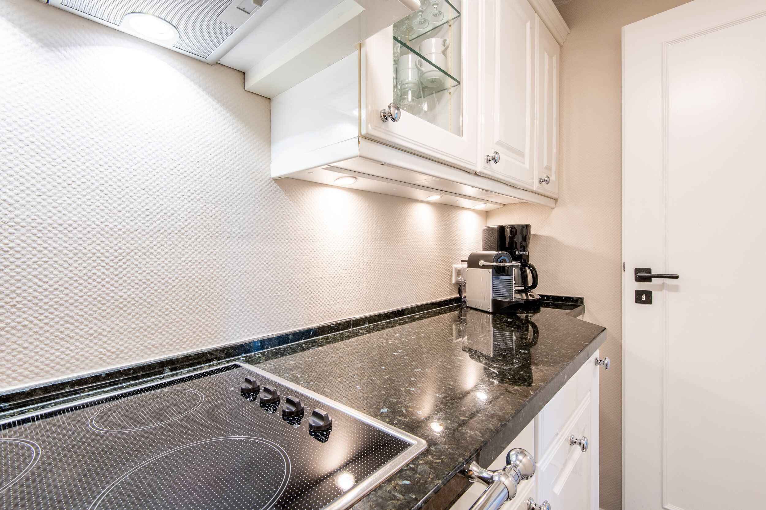 A kitchen with a black granite countertop, white cabinets, and a glass-fronted upper cabinet.