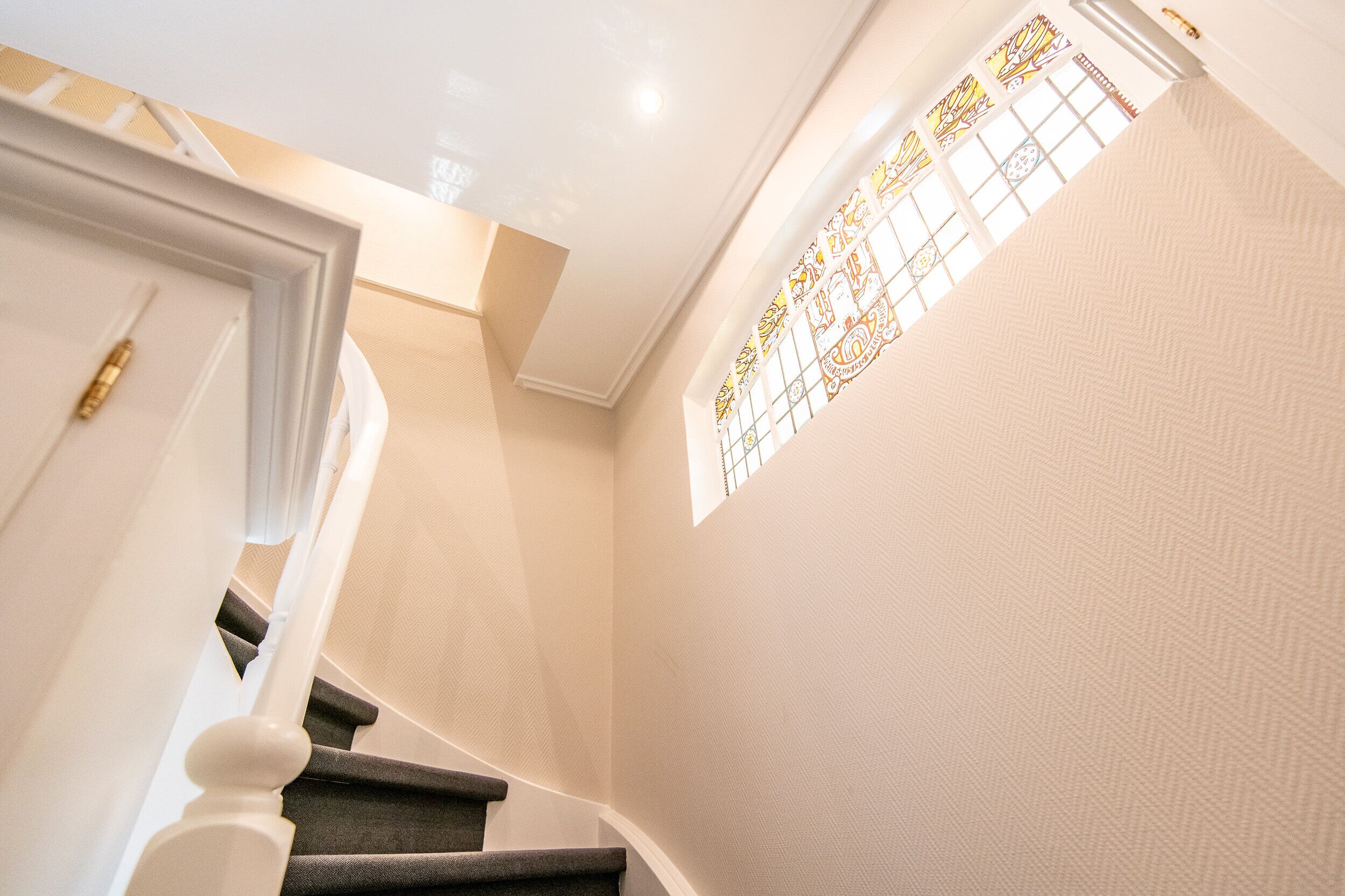 A staircase with a white door at the top and a stained glass window on the right.
