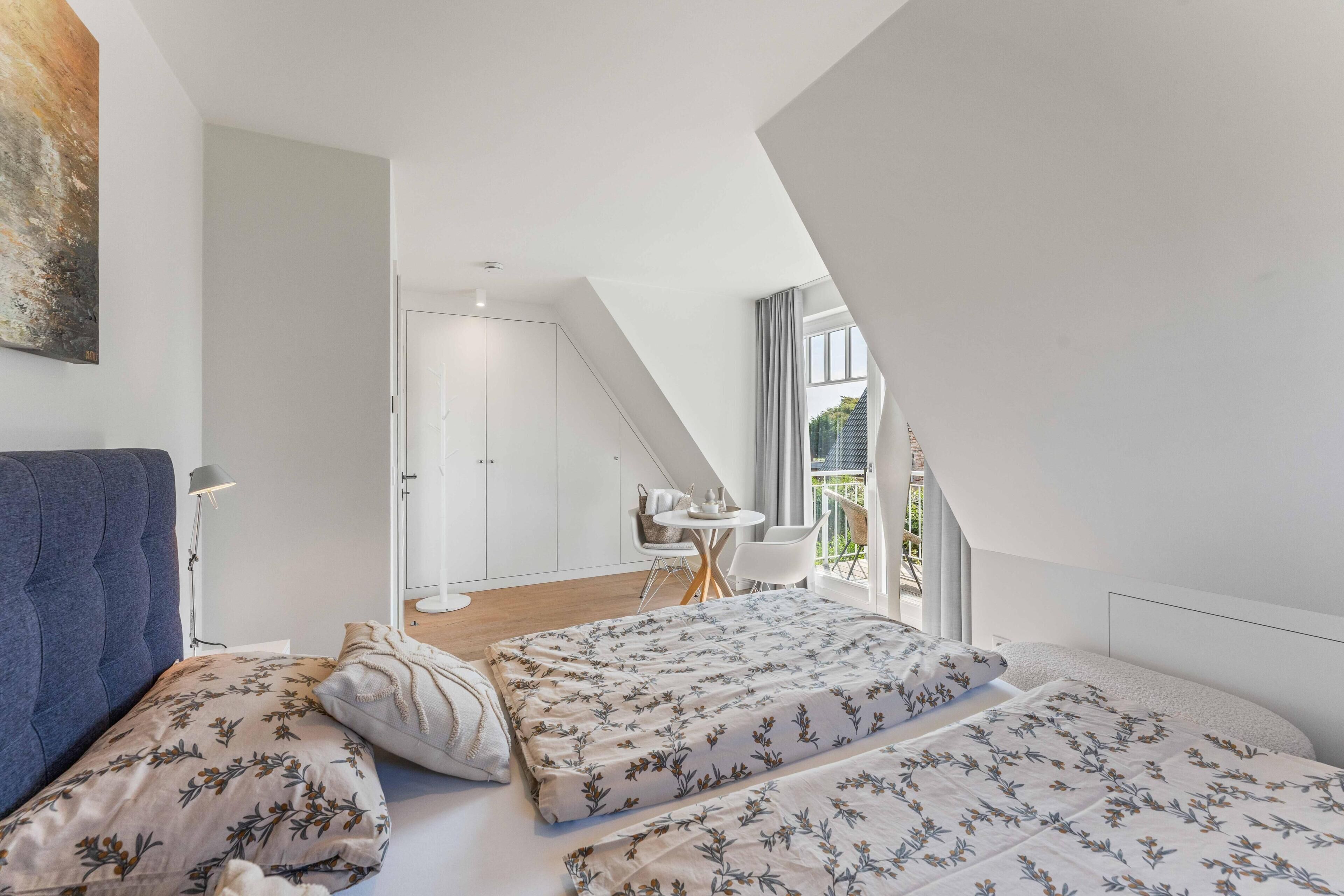 A bedroom with a bed, a chair, a table, and a view of the outdoors.