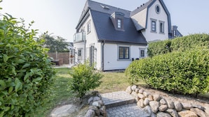 Kaksikerroksinen talo, jossa on jyrkkä katto, pieni kattoluukku ja kivestä tehty polku, joka johtaa sisäänkäynnille.