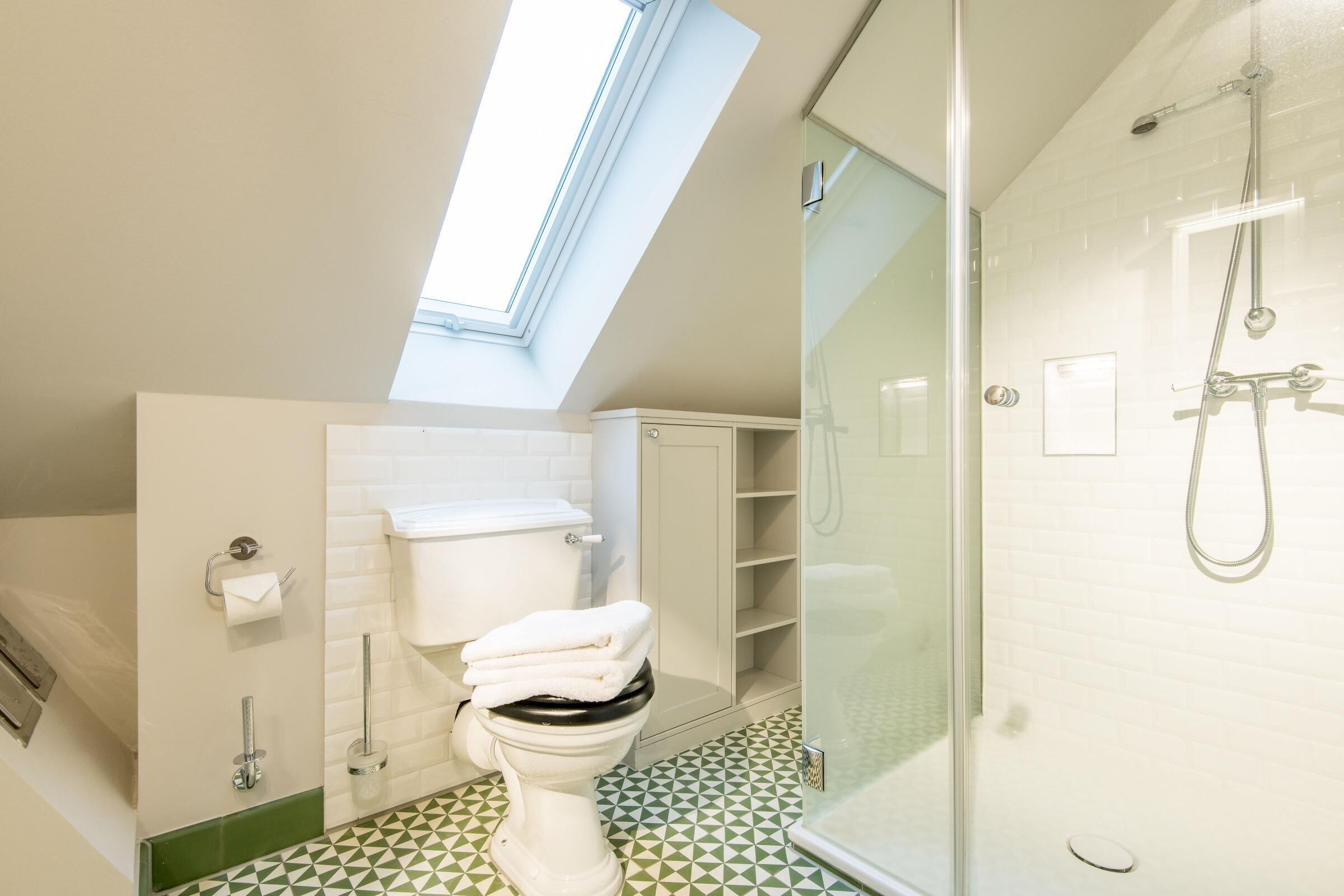 Ein modernes Badezimmer mit Dachfenster, einer gläsernen Dusche und einem WC mit Stauraum.