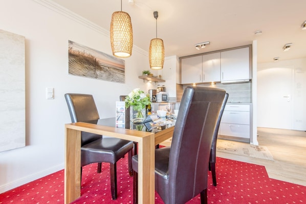Un espace repas comprenant une table en bois, des chaises en cuir noir et un tapis rouge à motifs.
