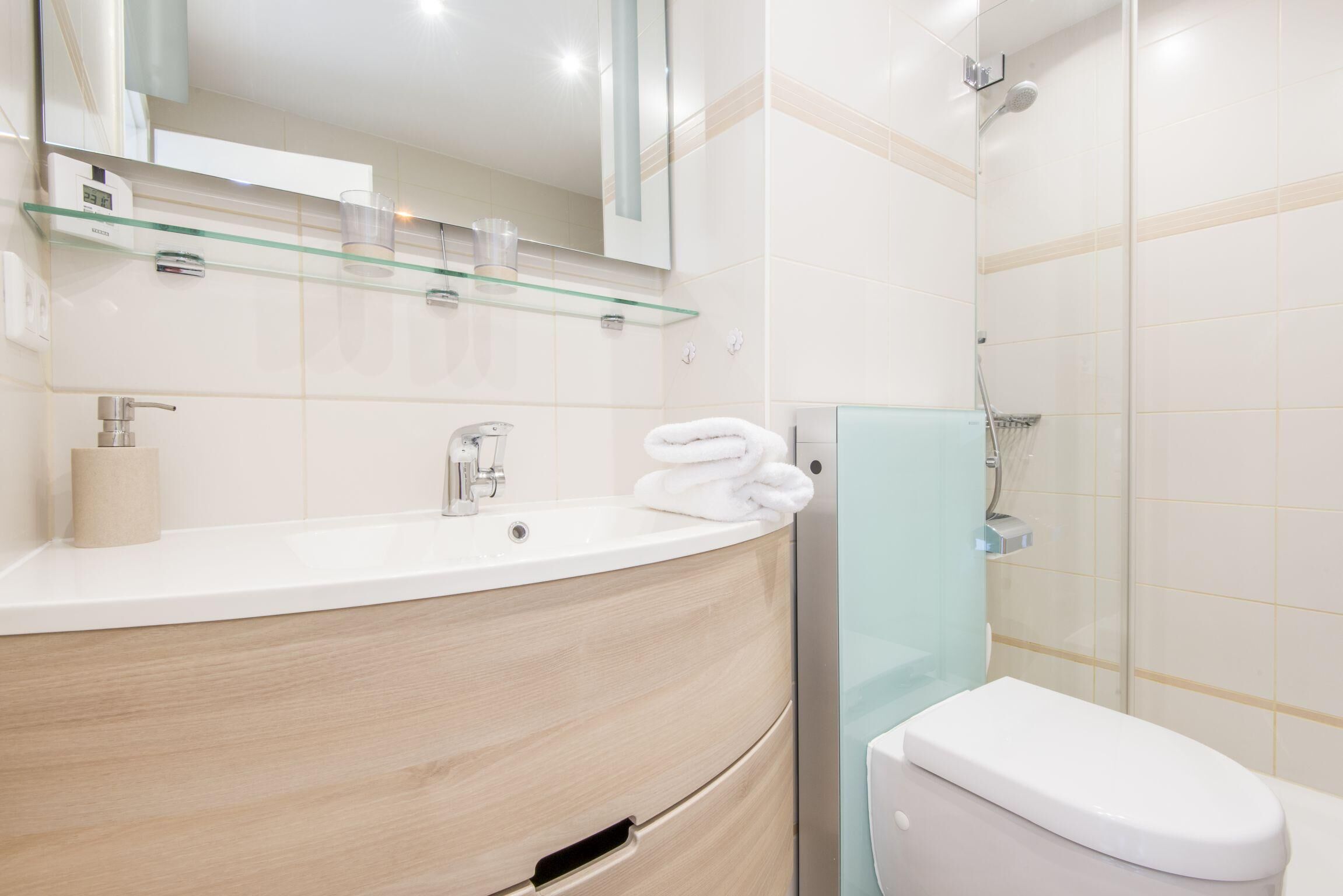 Een moderne badkamer met een gebogen wastafel, een glazen plank, een toilet en een douchehoek.